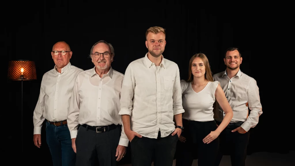 Team der Hausverwaltung Living zeigt 5 Mitarbeiter mit weißem Oberteil und schwarzer Hose. Es sind drei männliche Personen von links nach rechts, dann kommt eine weibliche Person und dann noch eine männliche Person.